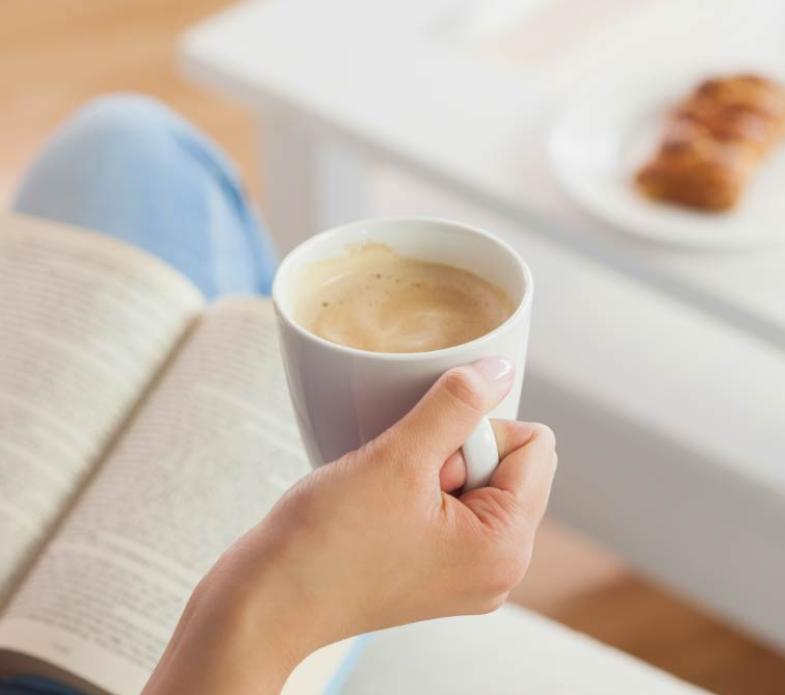 Persona legge un libro con una tazza di caffè.