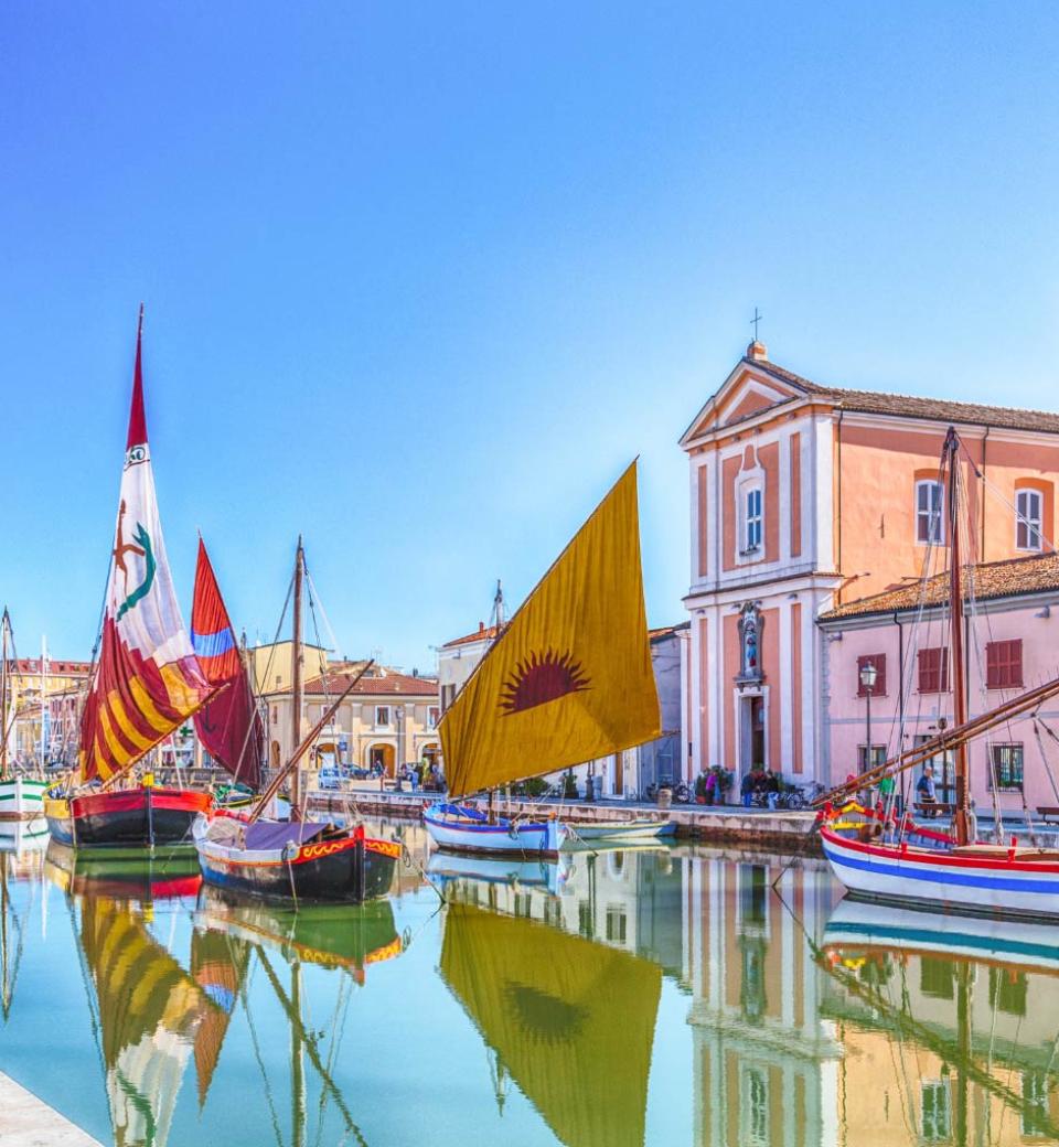Barche colorate con vele riflettenti in un canale vicino a un edificio storico.